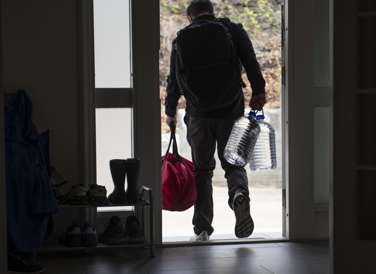 Man leaving his home carrying a bag and cans of water